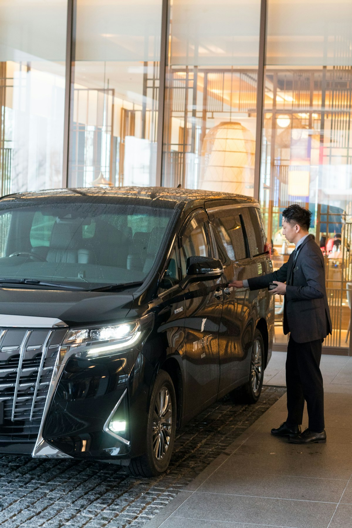 Chauffeur in a dark suit opening the door of a black luxury vehicle at a hotel entrance